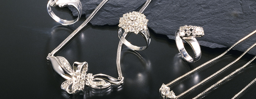 Collection of silver jewelry including rings, necklaces, and a brooch with clear gemstones on a dark reflective surface