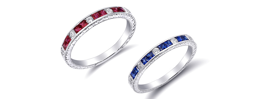 Two white metal eternity rings with red gemstones and blue gemstones alternating with clear stones, on white background