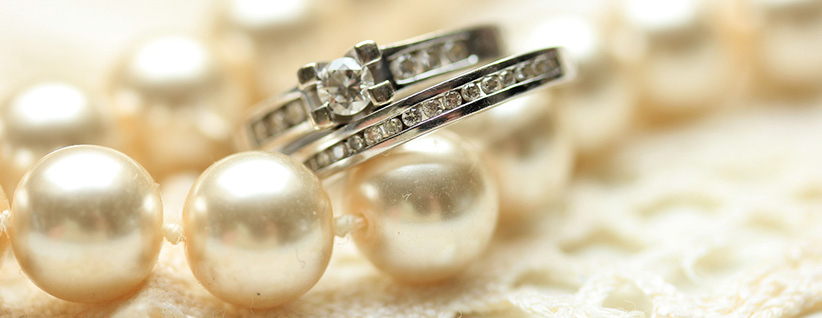 Close-up of diamond rings resting on a strand of pearls, cream and silver tones